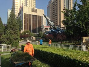 Frühmorgendliche Gartenarbeiter, im Hintergrund ein Luftwaffendenkmal